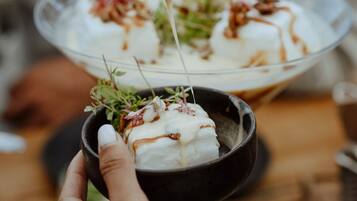 A person serving a dessert with a spoon, garnished with herbs and sauce, in a clear bowl.