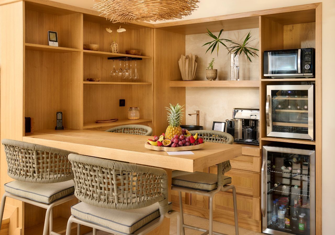 Una cocina moderna con una isla central, sillas de mimbre, estantes empotrados y un refrigerador.