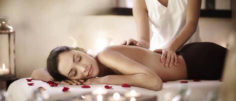 A massage therapy session with a client lying face down on a massage table, surrounded by candles and rose petals.