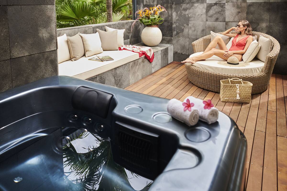 A spa area with a hot tub, a wicker lounge chair, and a seating area with cushions and a vase of flowers.