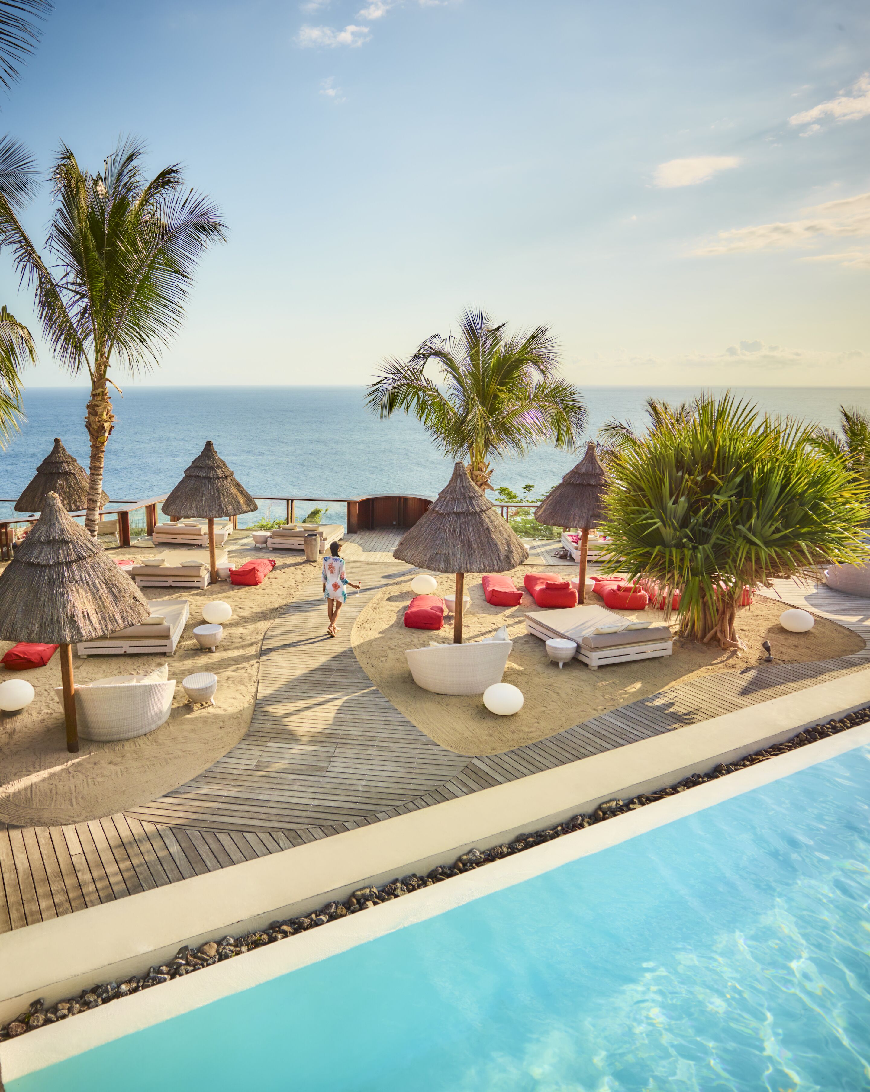 A resort pool area with thatched umbrellas, lounge chairs, and a clear view of the ocean.