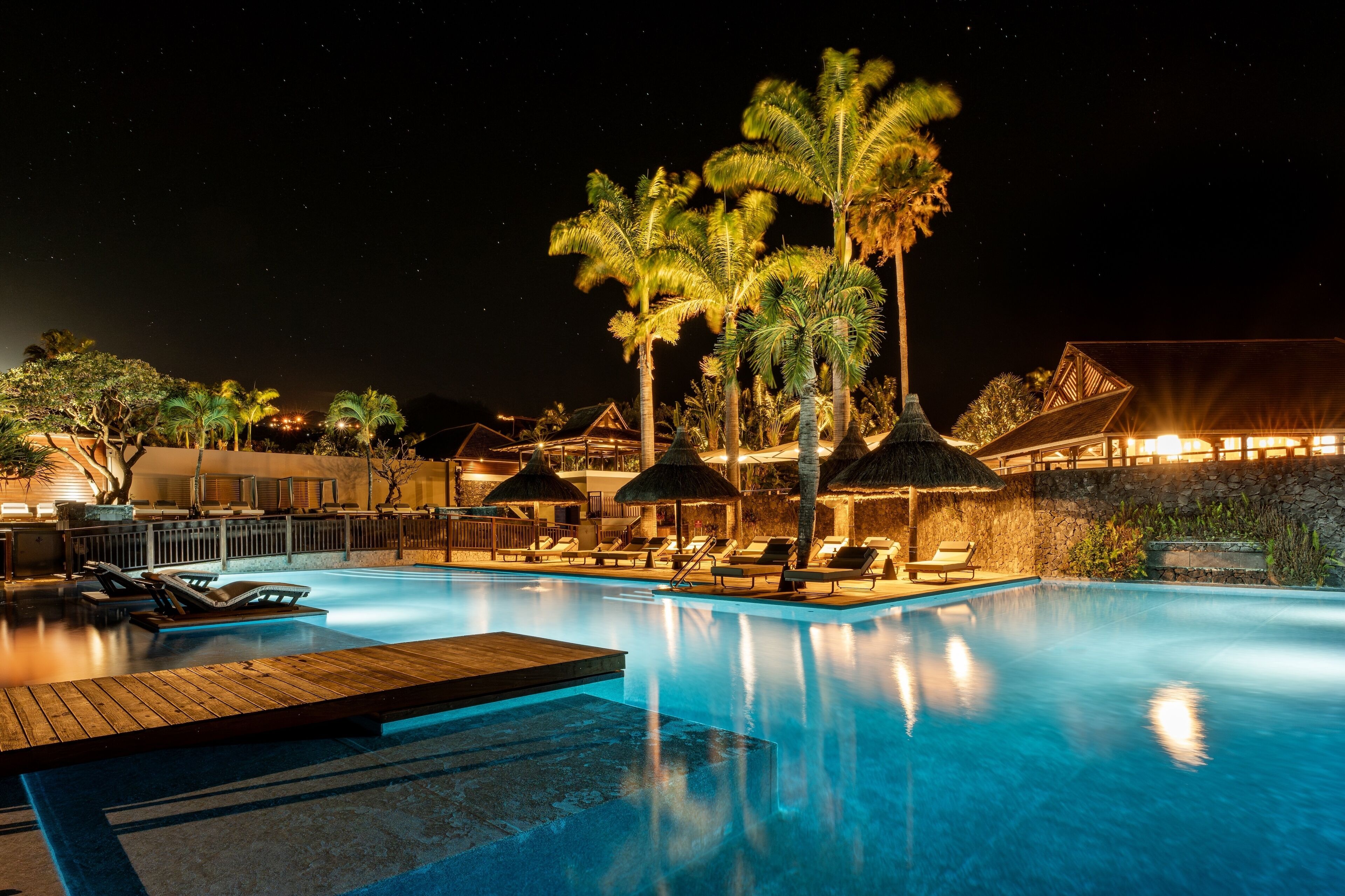 A nighttime swimming pool area with lounge chairs and palm trees.
