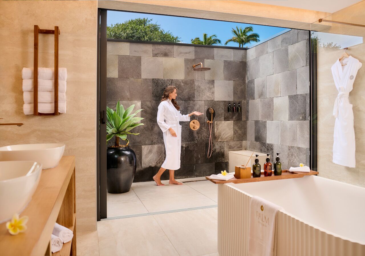 A modern bathroom with a large bathtub, a wooden towel rack, a potted plant, and a vanity with toiletries.
