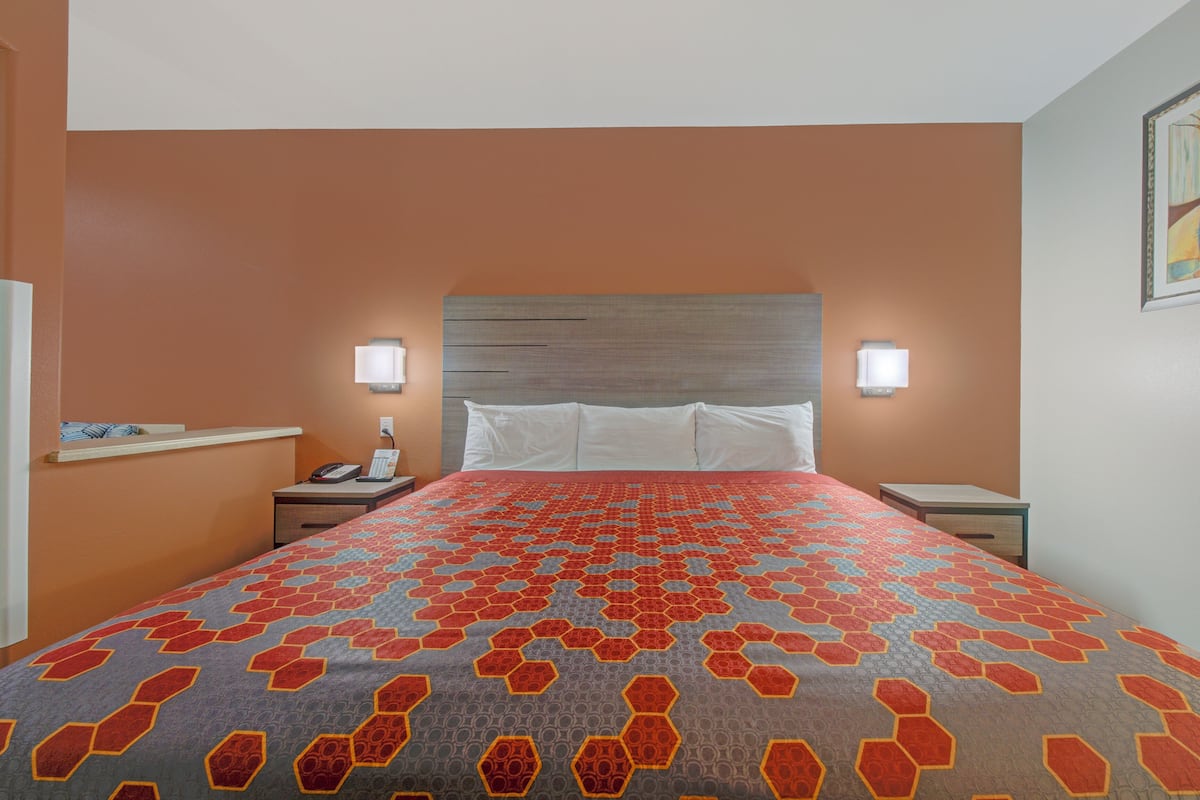 Une chambre d’hôtel avec un grand lit, deux tables de chevet, une petite table et une lampe fixée au mur.