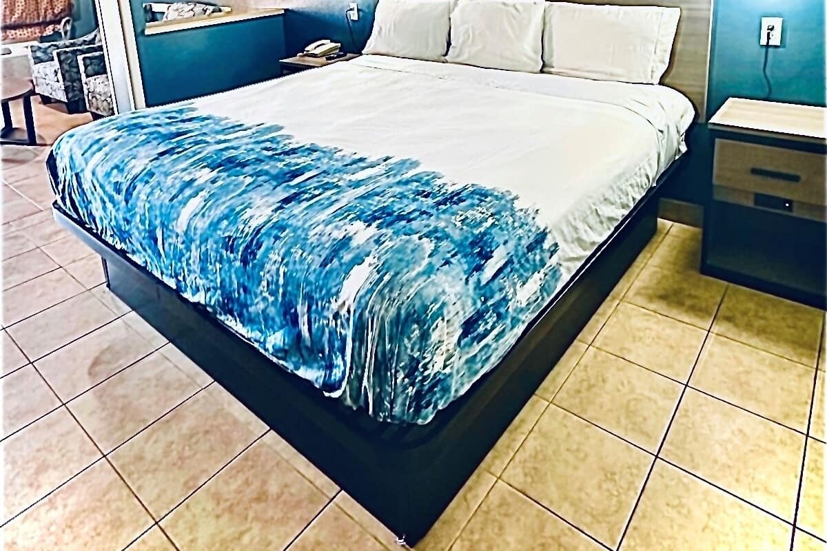 Une chambre d’hôtel avec un grand lit, une tête de lit en bois, une table de chevet et une lampe fixée au mur.