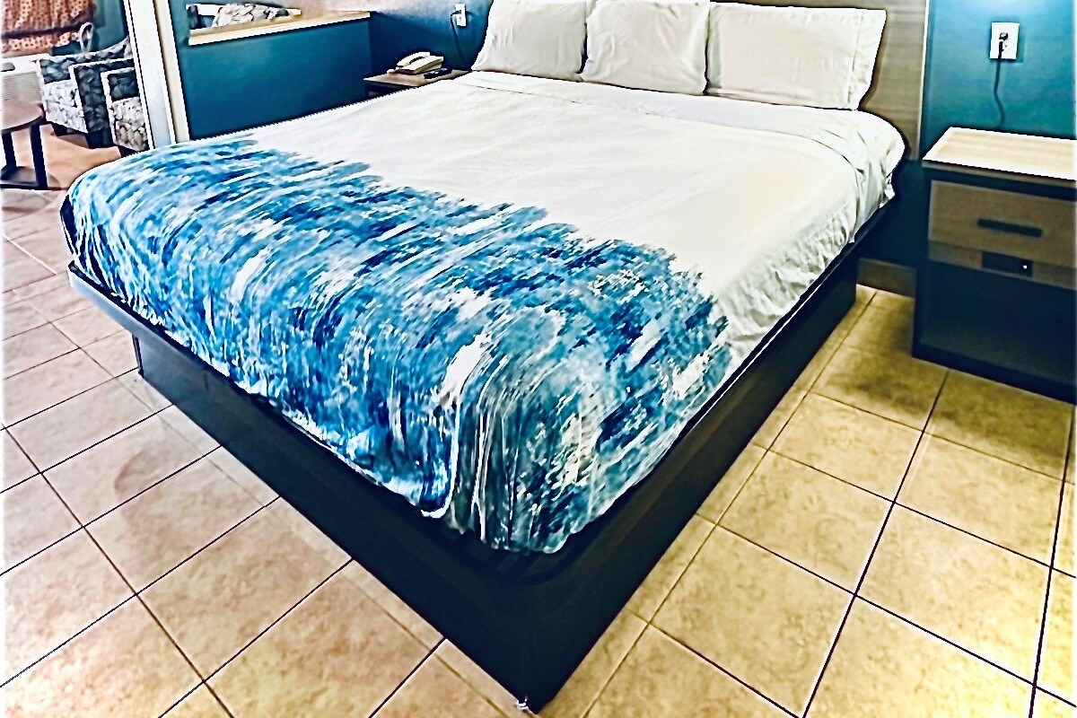 A hotel room with a large bed, a wooden headboard, a nightstand, a bedside table, and a wall-mounted lamp.