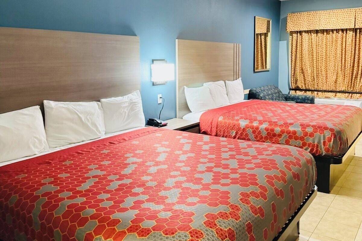 Une chambre d’hôtel avec deux lits, une table de chevet, une lampe et une fenêtre avec des rideaux.