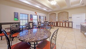 A spacious dining area with multiple round tables and chairs, a stone wall, and a reception desk. - Weslaco Inn Weslaco/Mercedes (Weslaco)