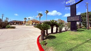 A hotel sign, a parking lot, and a building with a tiled roof. - Weslaco Inn Weslaco/Mercedes (Weslaco)