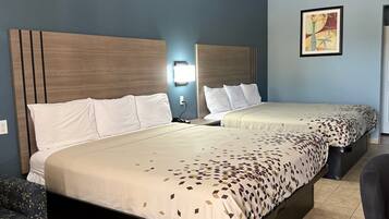 A hotel room with two beds, a desk, a chair, and a wall-mounted light.