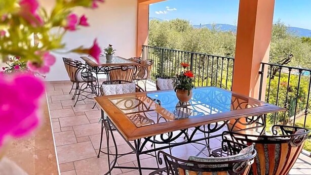 A balcony with outdoor furniture, a view of greenery and mountains, and a clear sky. - Vittoria (Toscolano Maderno)