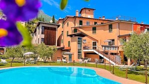 A hotel with a swimming pool, outdoor seating, and a mountainous backdrop. - Vittoria (Toscolano Maderno)