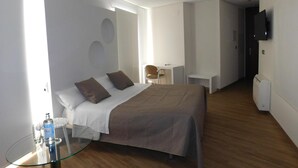 A modern hotel room with a large bed, a glass table with a bottle, a desk, and a TV mounted on the wall. - Hospedium Hotel Cañitas Maite Boutique (Casas-Ibanez)