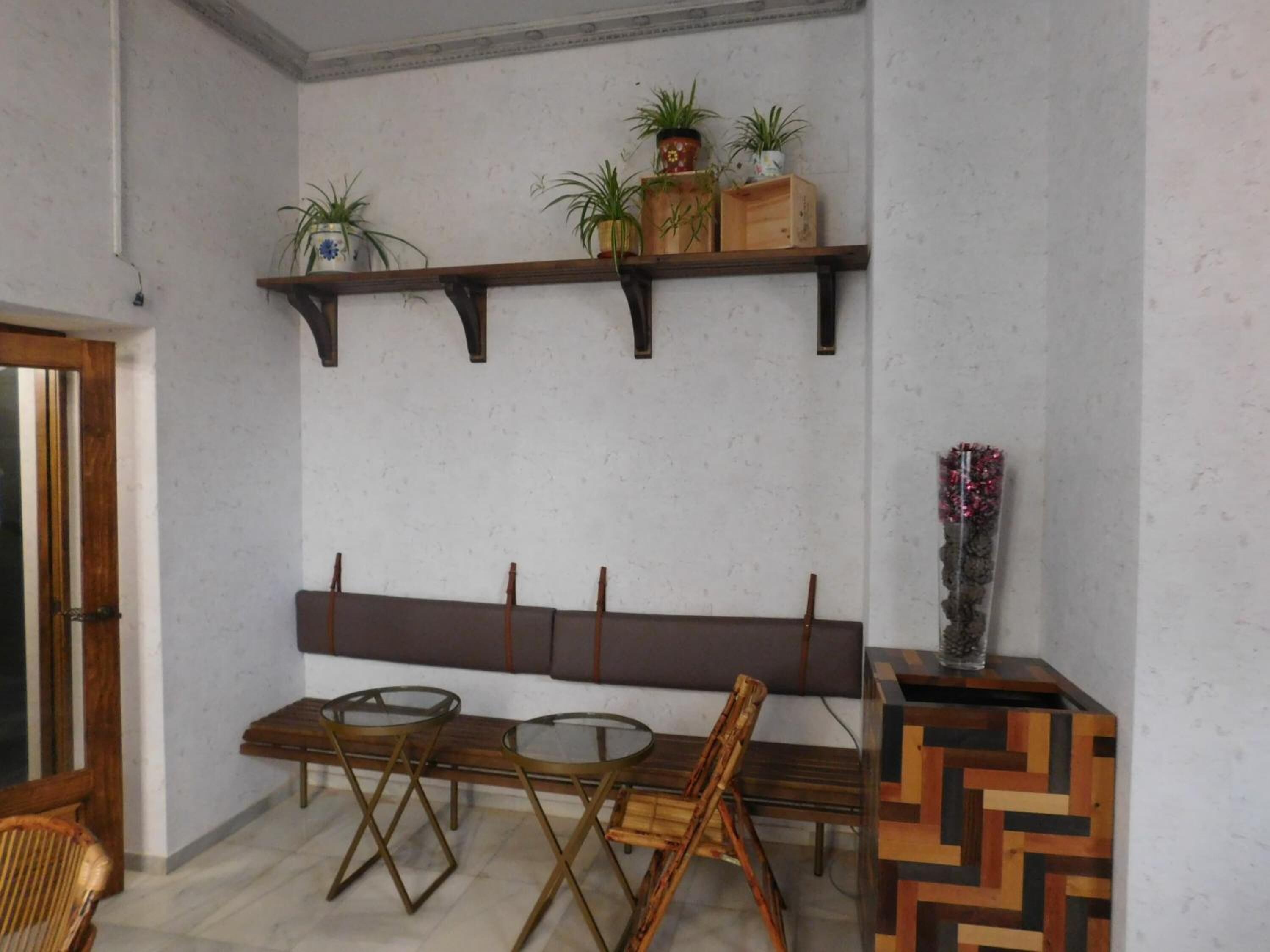 Un coin repas comprenant un banc en bois, deux tables en verre et un vase décoratif.