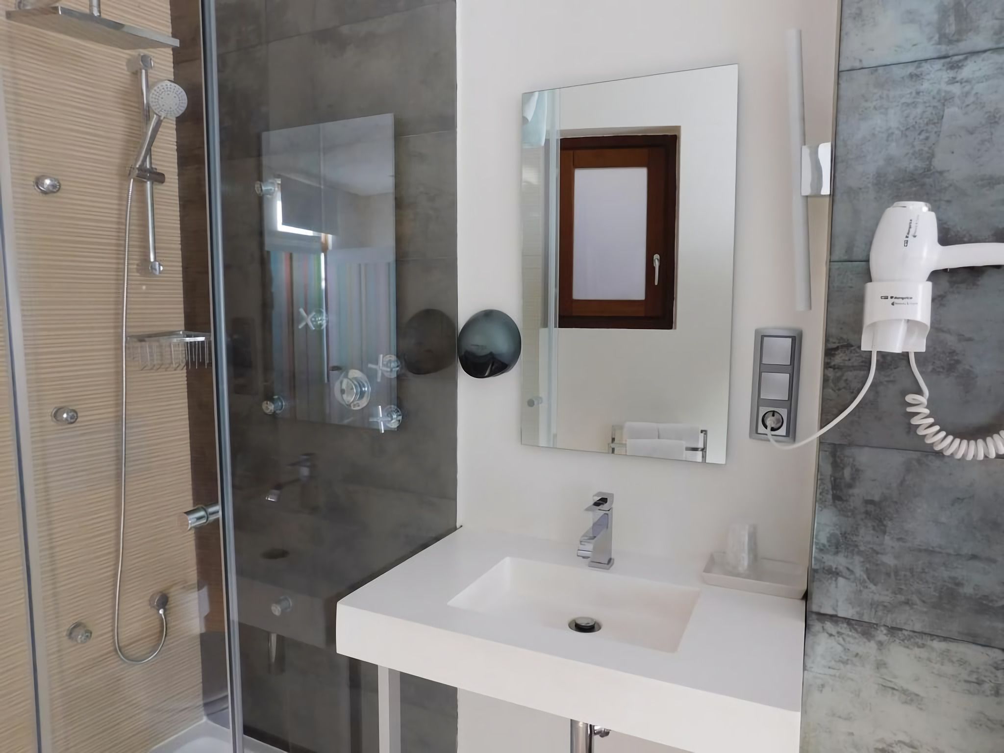 Casa de banho moderna com cabine de duche em vidro, lavatório branco e secador de cabelo fixado na parede.