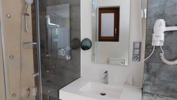 Casa de banho moderna com cabine de duche em vidro, lavatório branco e secador de cabelo fixado na parede.