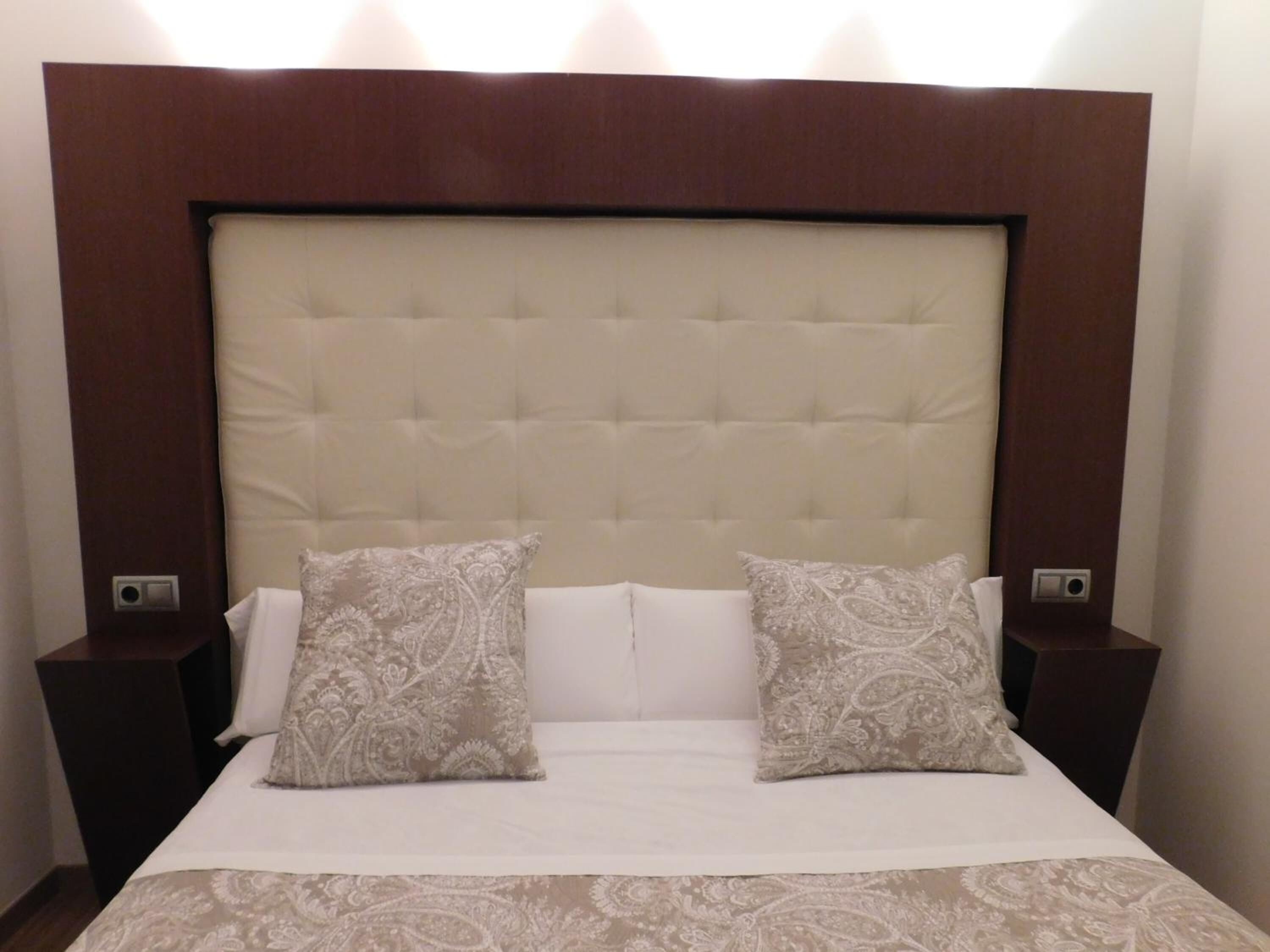 Une chambre d’hôtel avec une tête de lit capitonnée, deux coussins à motifs et un couvre-lit blanc.