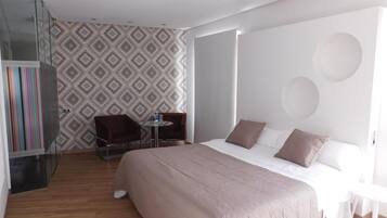 A modern hotel room with a large bed, a glass wardrobe, a small round table, and a patterned wall.