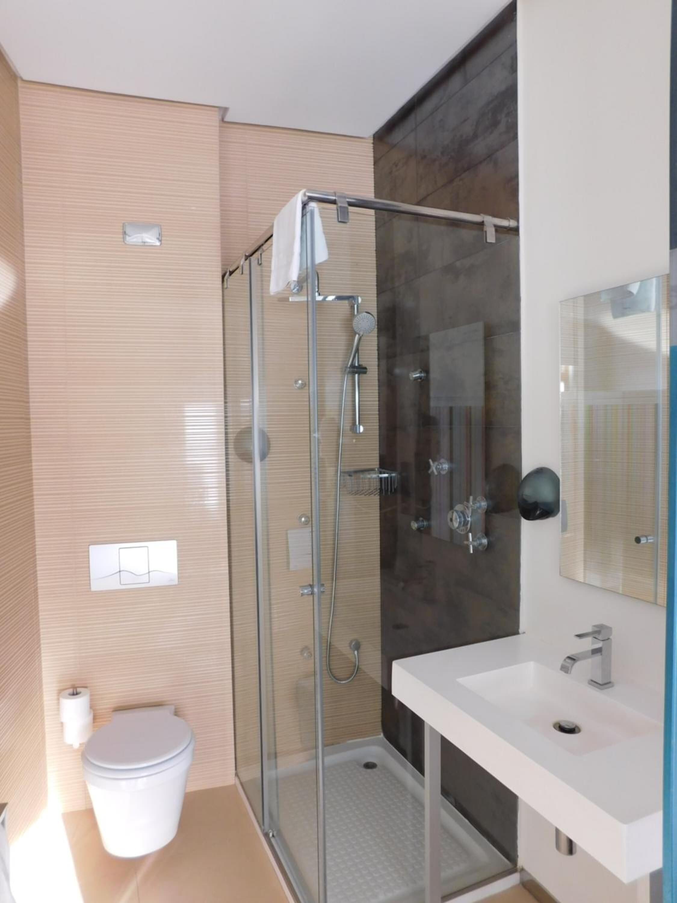 Un baño moderno con ducha de vidrio, lavamanos blanco y un espejo grande.