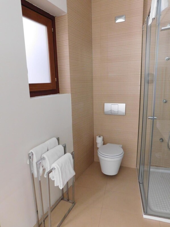 A bathroom with a toilet, a glass shower enclosure, and a towel rack with towels.