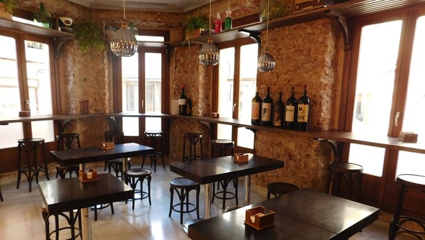 A restaurant interior with rustic stone walls, multiple tables and chairs, hanging pendant lights, and wine bottles on shelves. - Hospedium Hotel Cañitas Maite Boutique (Casas-Ibanez)
