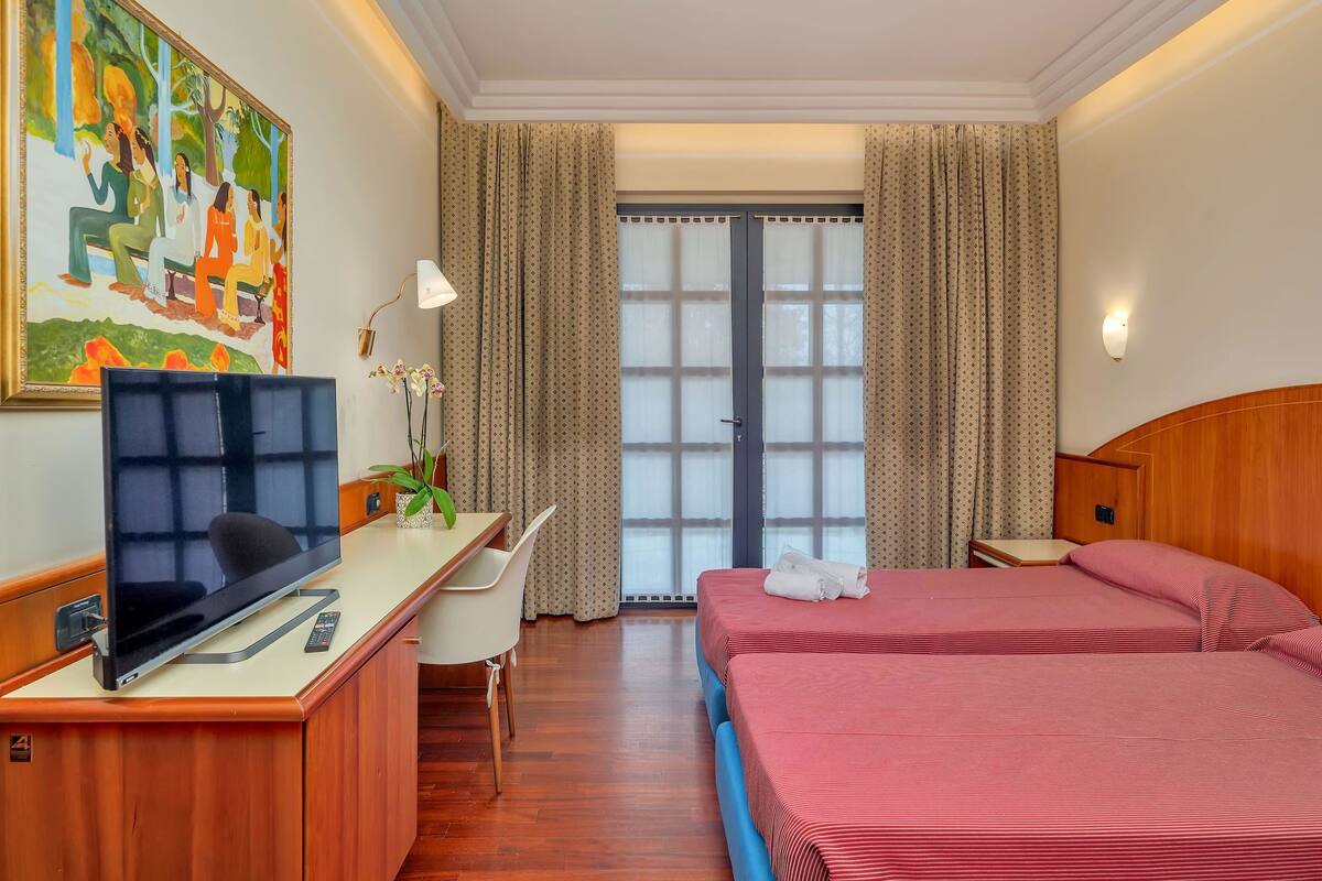 A hotel room with a bed, desk, chair, TV, and a painting on the wall.