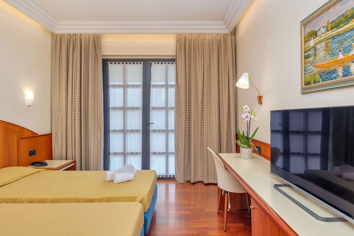 A hotel room with a bed, desk, TV, and curtains.