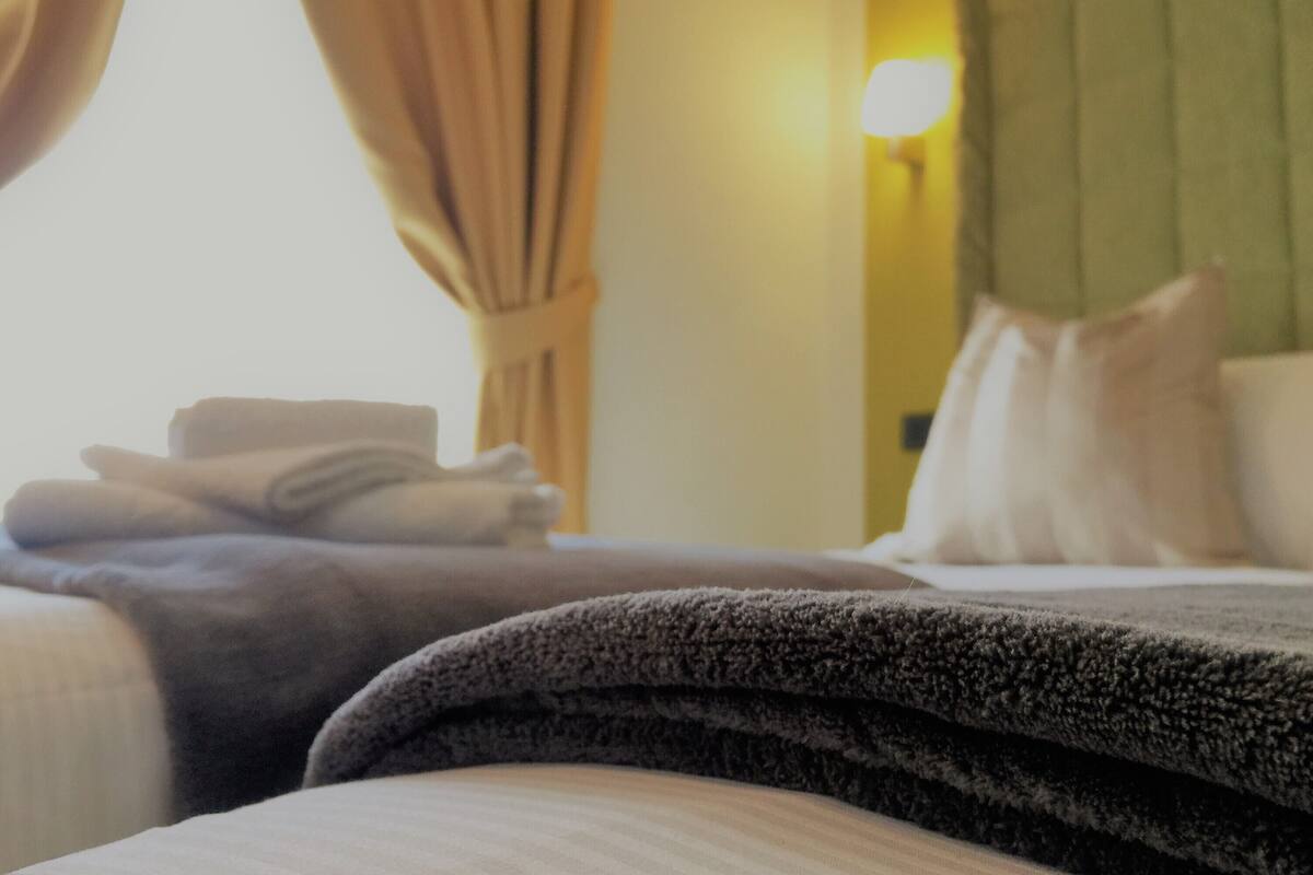 Una habitación de hotel con una cama bien hecha, cabecera verde y una lámpara en la pared.