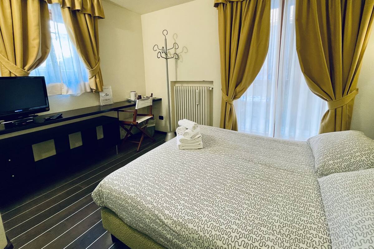 Una habitación de hotel con cama, escritorio y televisor, además de cortinas.