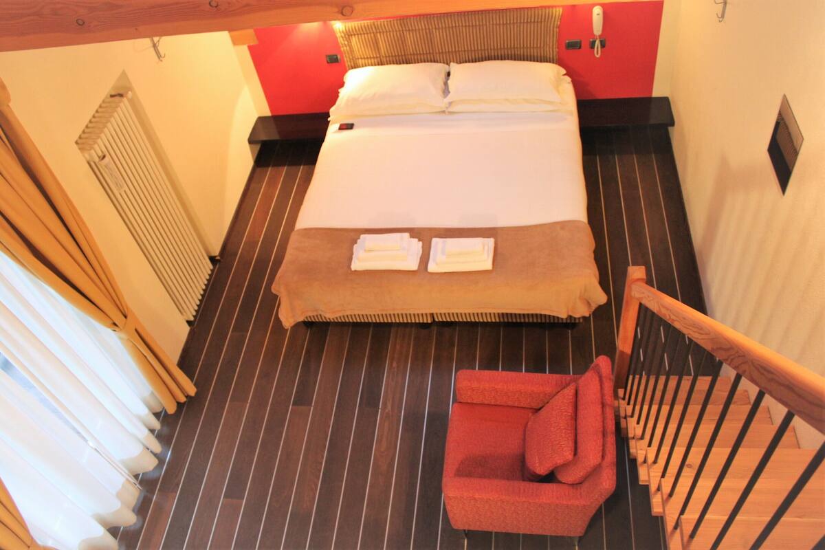 Una habitación de hotel con una cama, una silla roja y una escalera de madera.