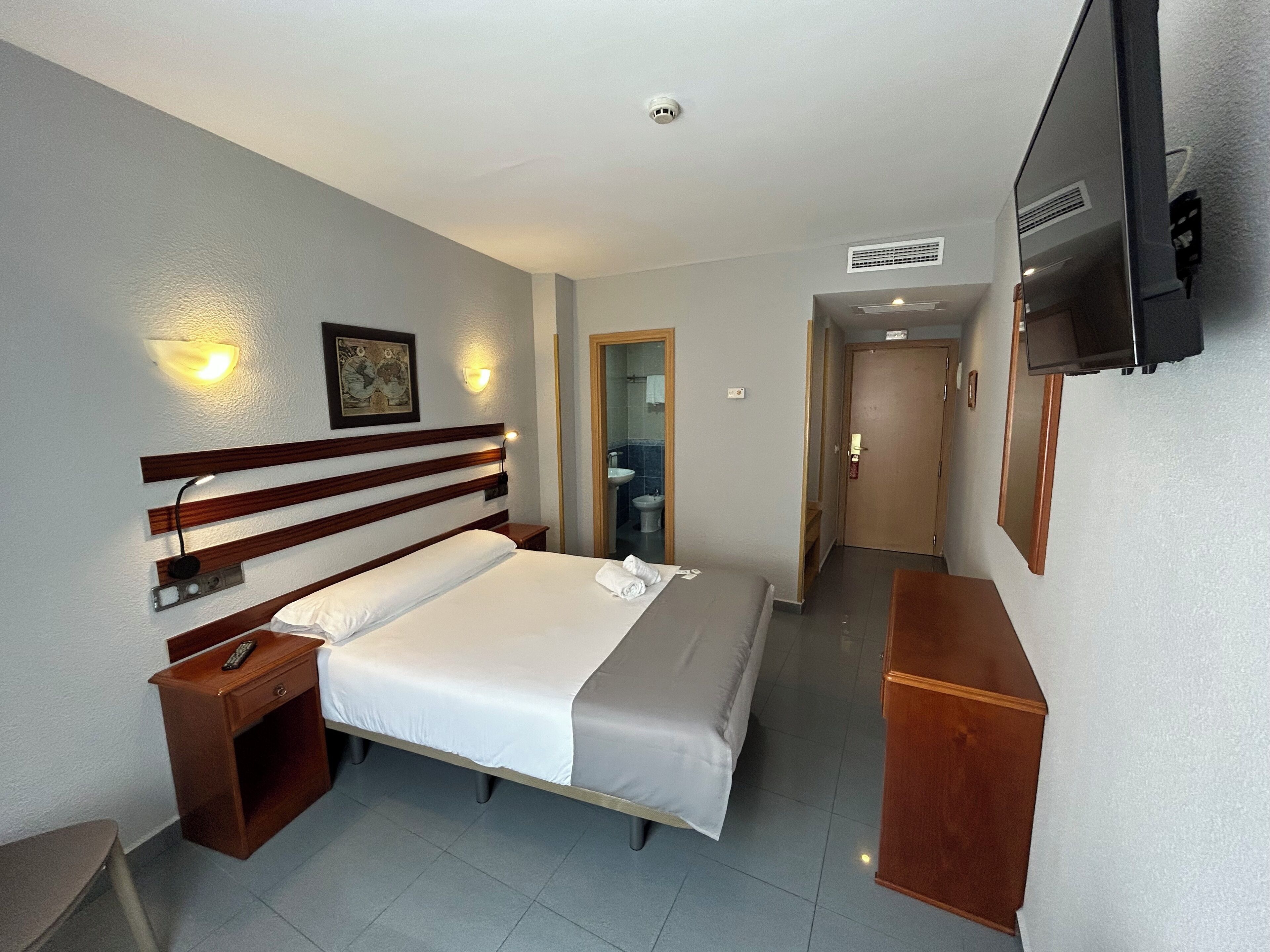 A hotel room with a bed, bedside table, TV, and a bathroom visible through an open door.