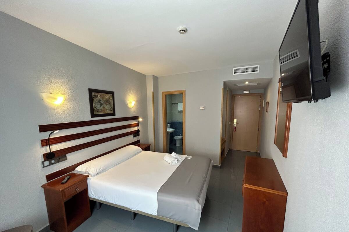 A hotel room with a bed, bedside table, TV, and a bathroom visible through an open door.