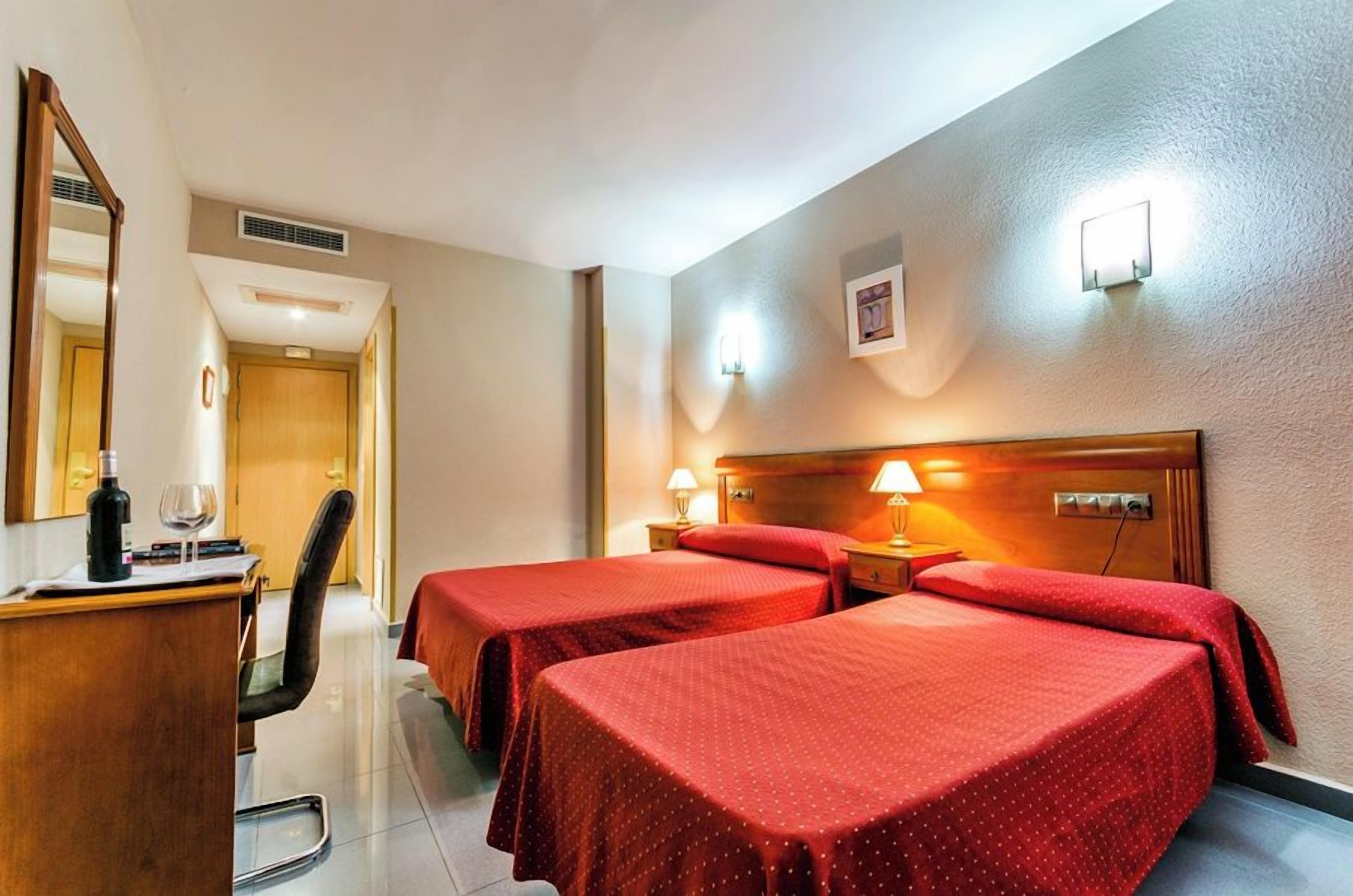 Een hotelkamer met twee eenpersoonsbedden, een bureau met stoel, een spiegel en een deur die naar een andere kamer leidt.
