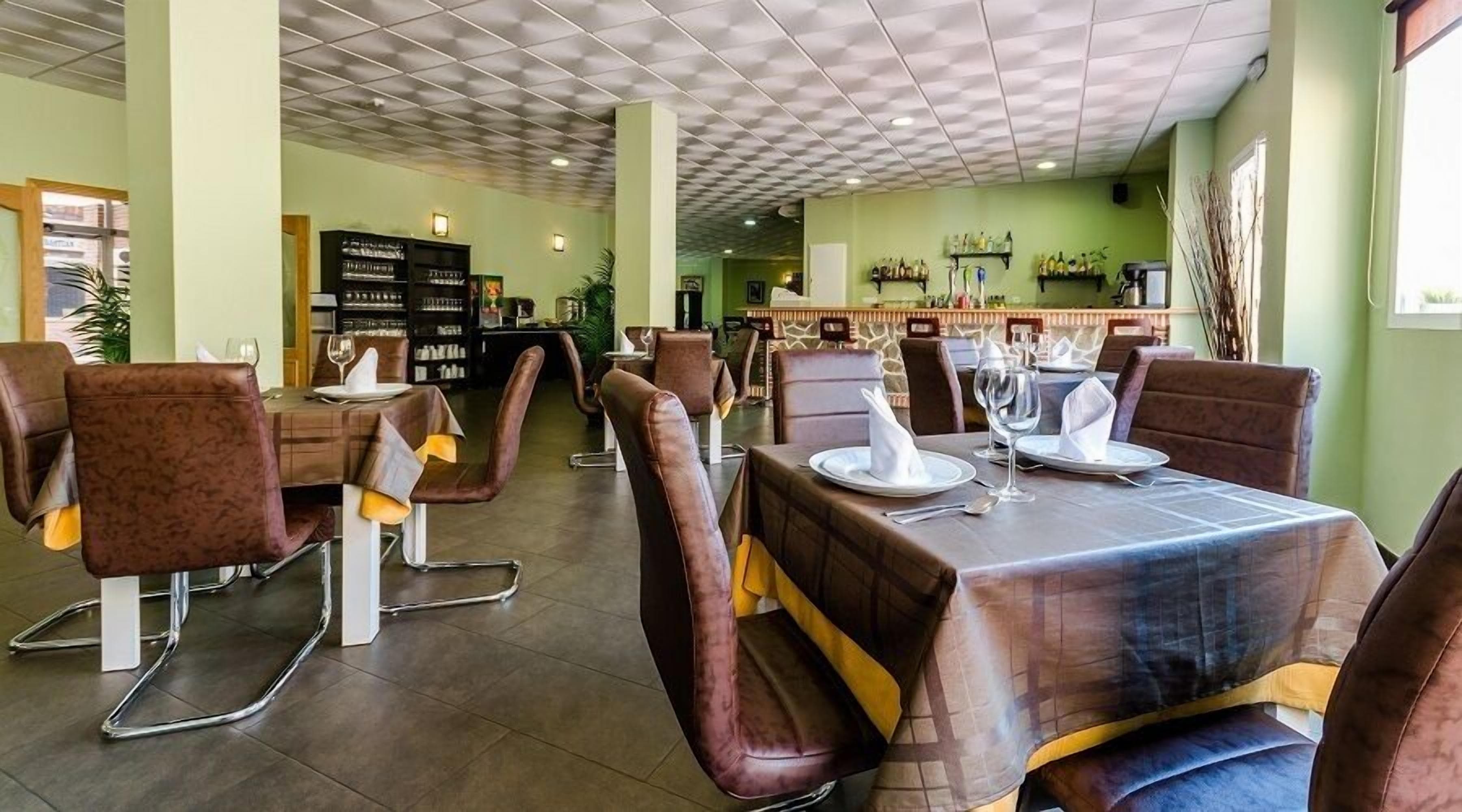 Ein Restaurant mit Sitzecken und hohen Tischen, einer Bar und einer grünen Wand mit Regalen.