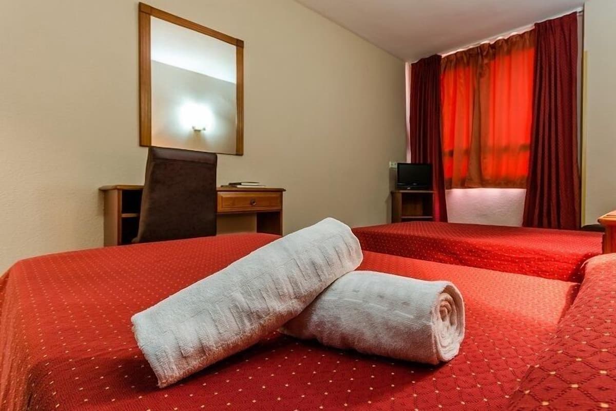 A hotel room with two beds, a desk, a chair, a TV, and a lamp.