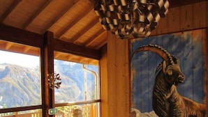 Una cabaña de madera con vista a la montaña, un cuadro decorativo de una cabra y una lámpara colgante única.