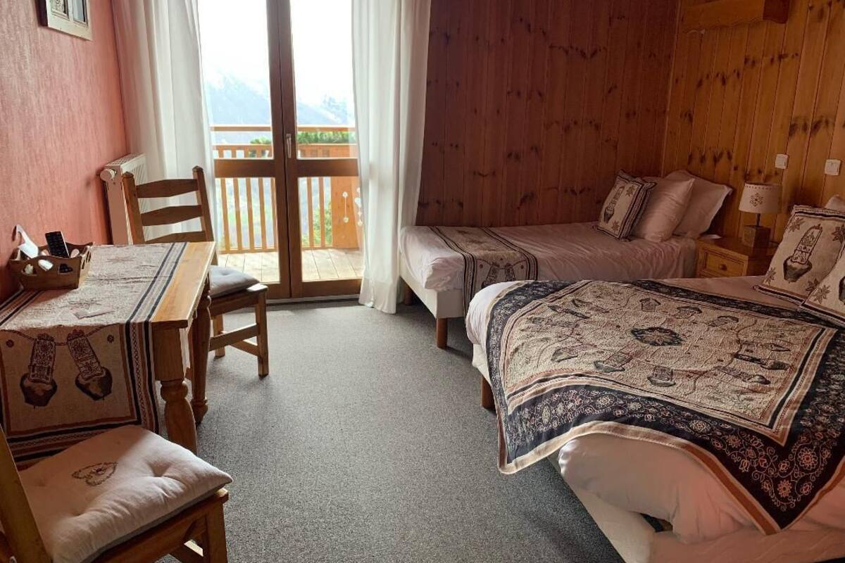 Een gezellige kamer met houten vloer, een bed met beddengoed met patroon, een kleine tafel met stoel, en een balkon met houten leuning.