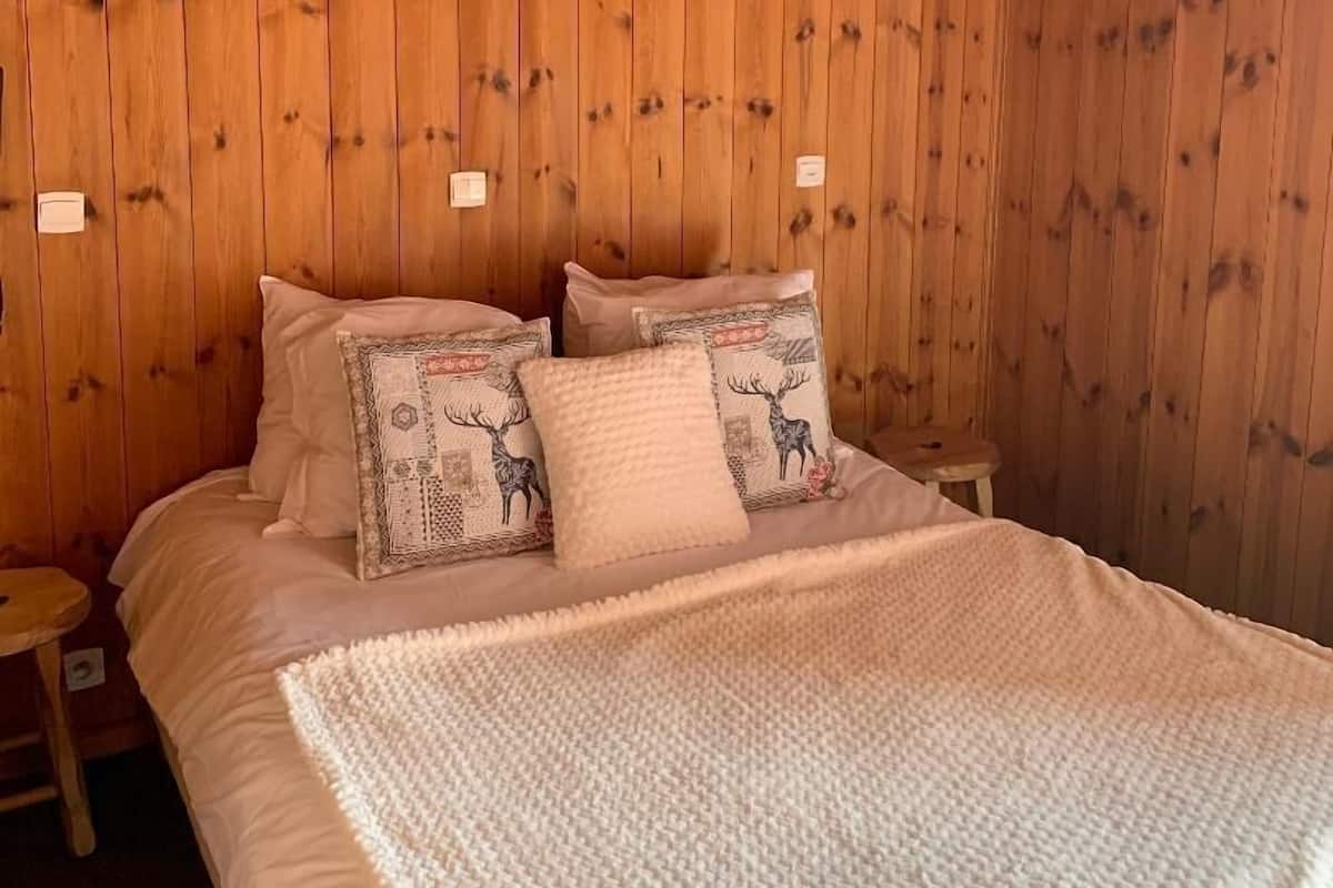 Een slaapkamer met houten lambrisering, een bed, kussens en een klein nachtkastje.