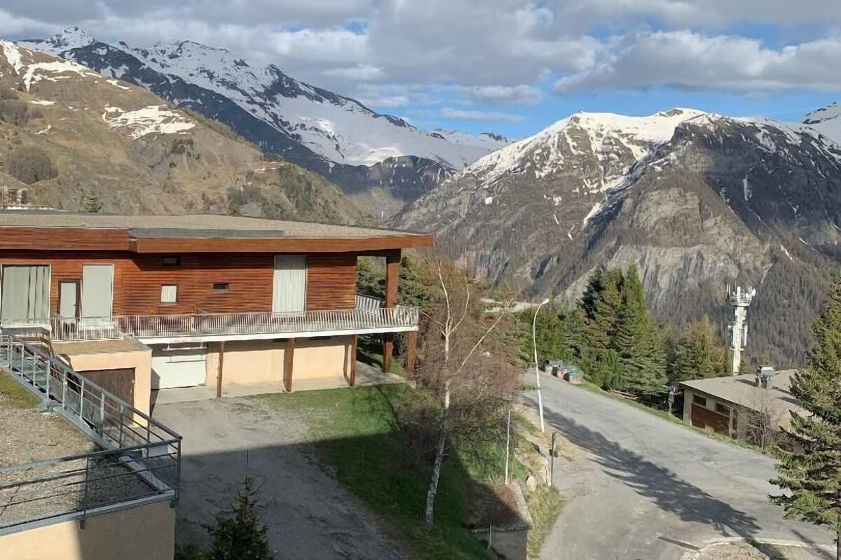 Een modern gebouw met balkon, omgeven door een bergachtig landschap en een heldere lucht.
