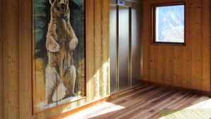 Un interior de madera con un mural de un oso, un ascensor y una ventana con vistas a la montaña.