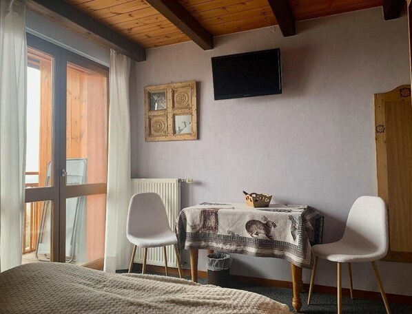 A room with a bed, a table with a tablecloth, two chairs, a radiator, a television, and a wooden door. - Hôtel Les Catrems (Orcieres)