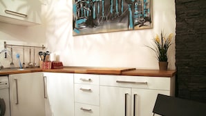 A modern kitchen with white cabinets, a wooden countertop, and a painting above the sink. - Apartment Berlin 1 (Berlin)
