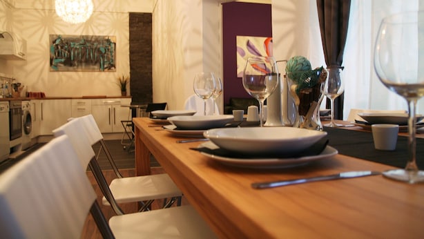 A dining area with a wooden table set for two, white chairs, and a view of the kitchen in the background. - Apartment Berlin 1 (Berlin)