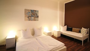 A bedroom with a large bed, a smaller sofa, bedside tables with lamps, and a painting on the wall. - Apartment Berlin 1 (Berlin)