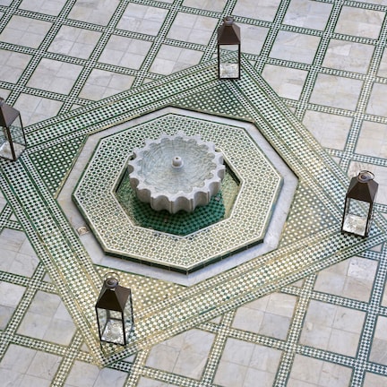 A geometric tiled floor with a central fountain and four lanterns.