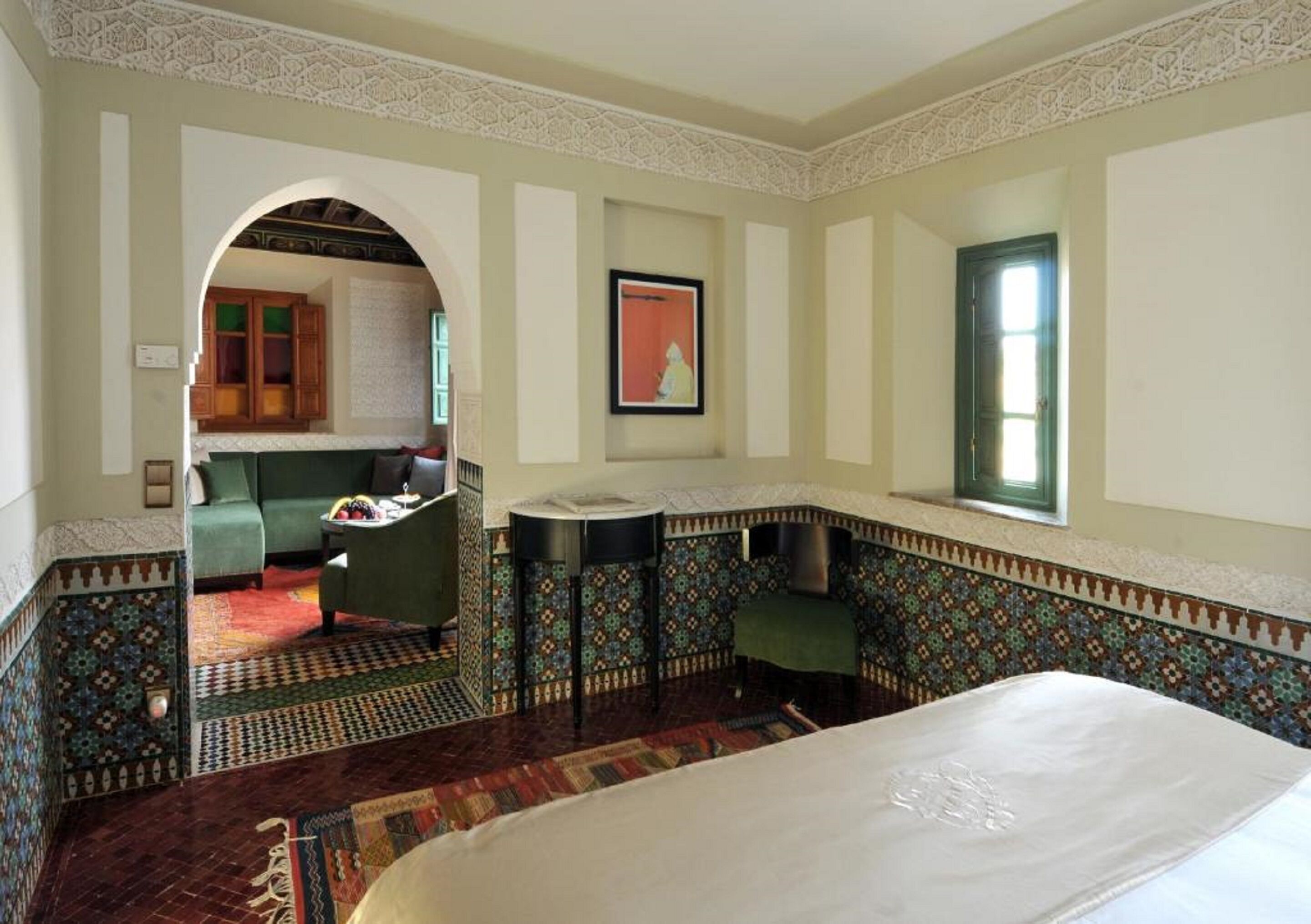 A room with a bed, a small table, a chair, a sofa, a kitchen area, and a patterned floor.