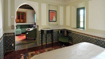 A room with a bed, a small table, a chair, a sofa, a kitchen area, and a patterned floor.