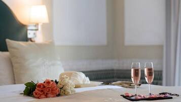Uma cama bem arrumada com um buquê de rosas e duas taças de champanhe em um suporte.