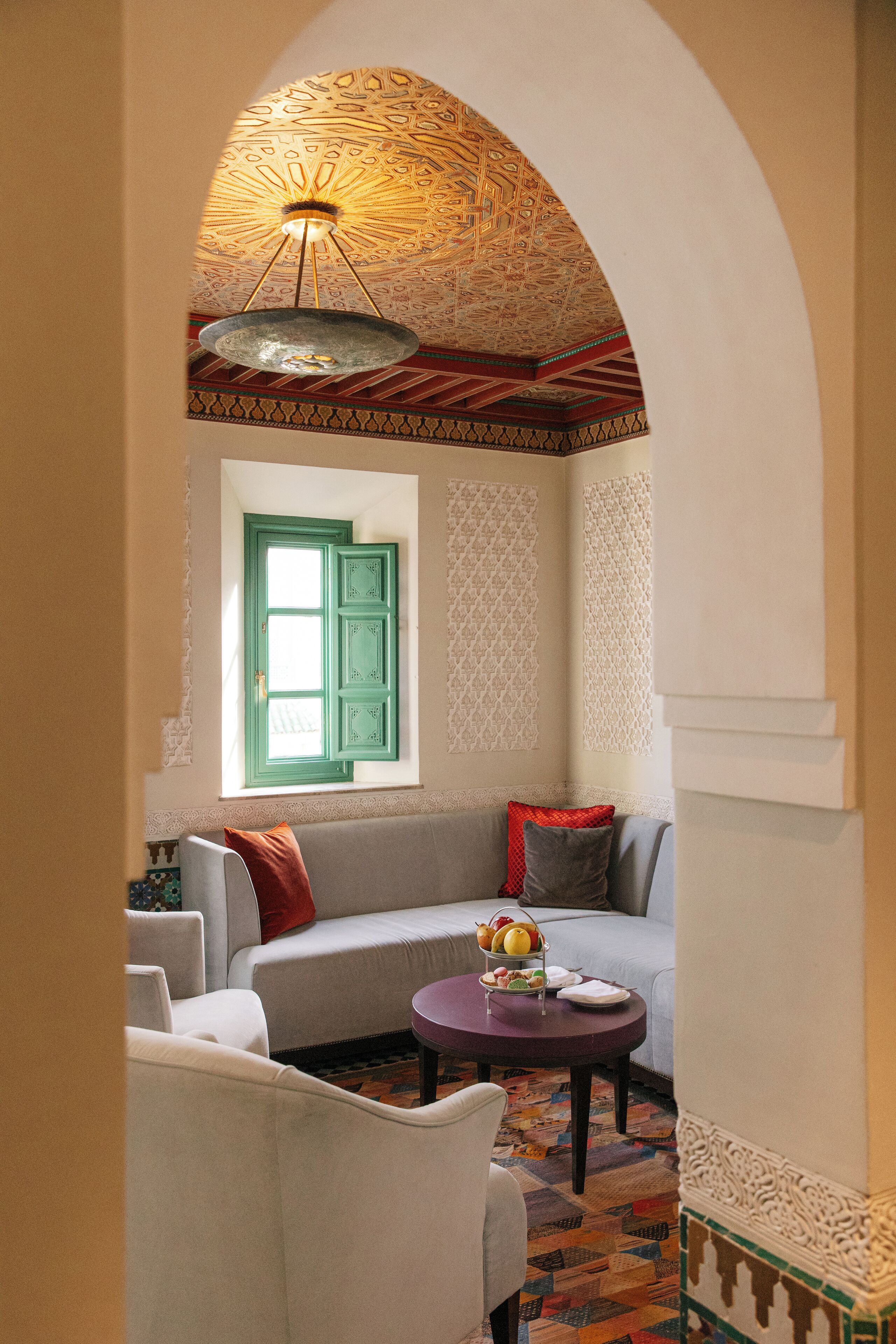 A cozy living room with a curved sofa, a round table with fruit, and a decorative ceiling.