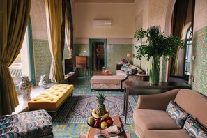 A spacious living area with a sofa, a bench, and a table with a fruit centerpiece.